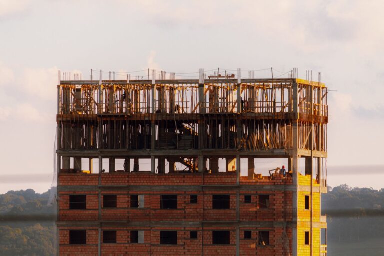 Brick building under construction at sunset with workers visible on top floor.