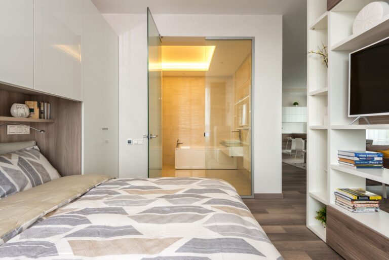 Interior of contemporary bedroom with white built in wardrobe and shelves behind bed and TV shelf against