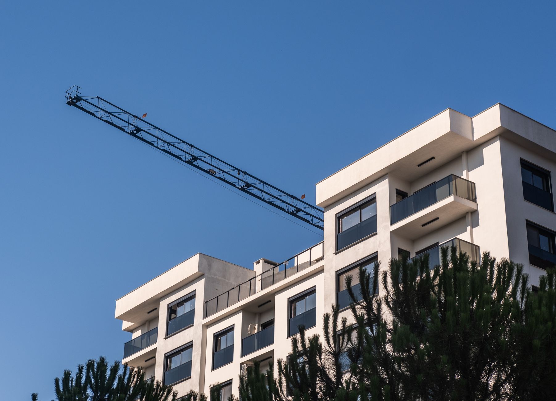 A modern apartment building in İzmir with a construction crane under a clear blue sky.