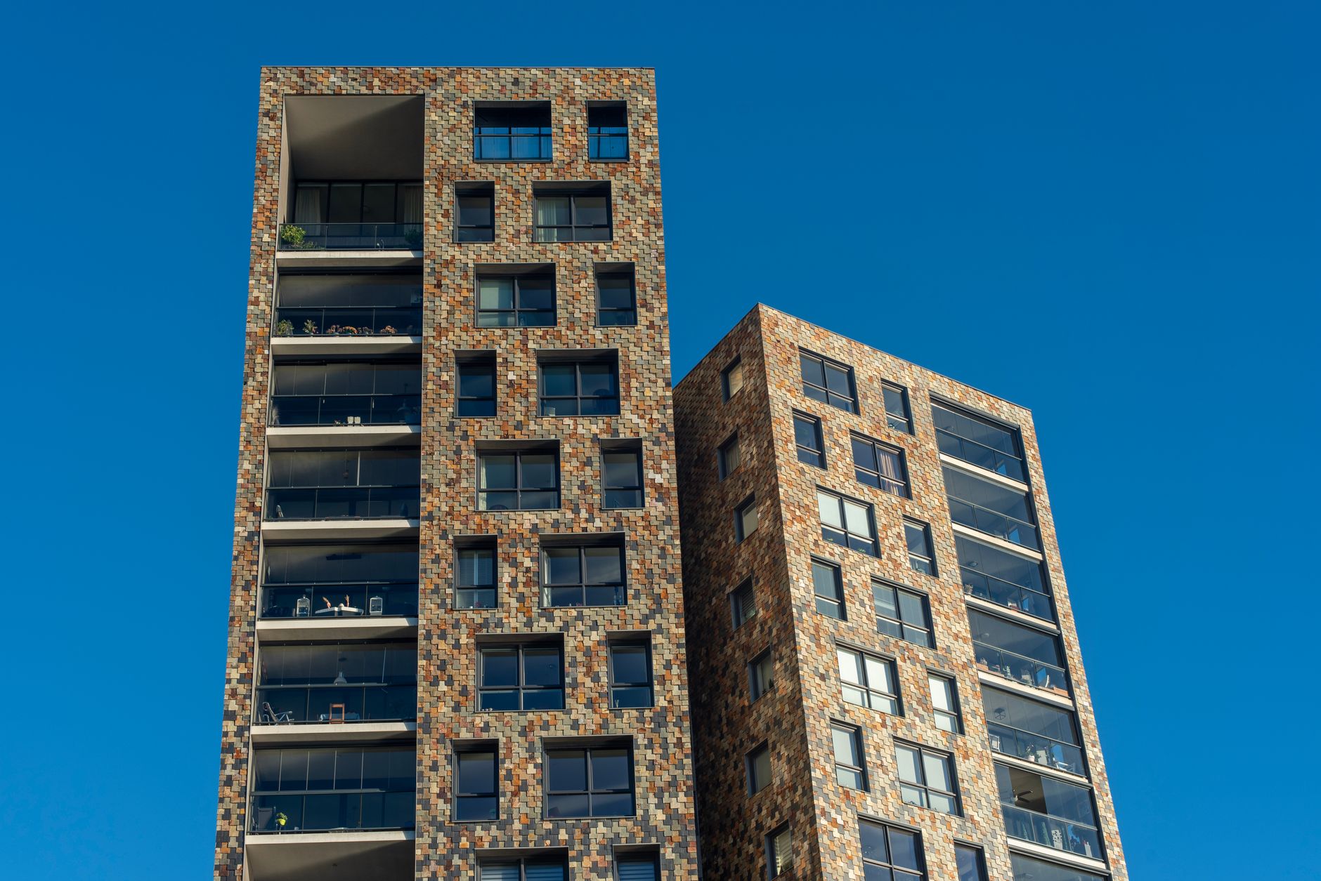 Two modern high-rise buildings with a brick facade against a clear blue sky.