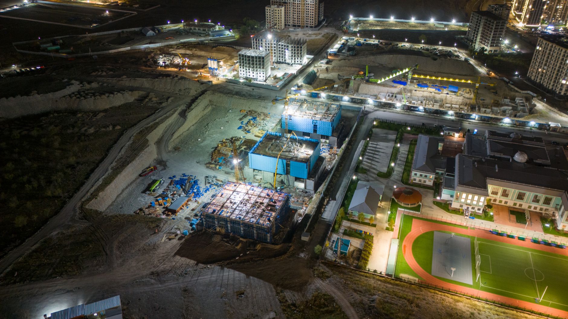 A vibrant aerial shot of a construction site at night with buildings and lights.