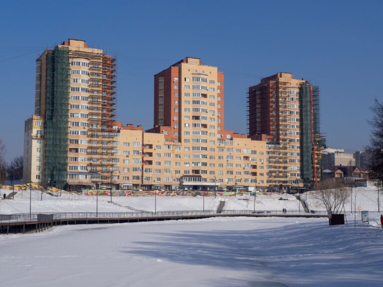 Urban high-rise apartment buildings under construction surrounded by snow on a clear winter day.