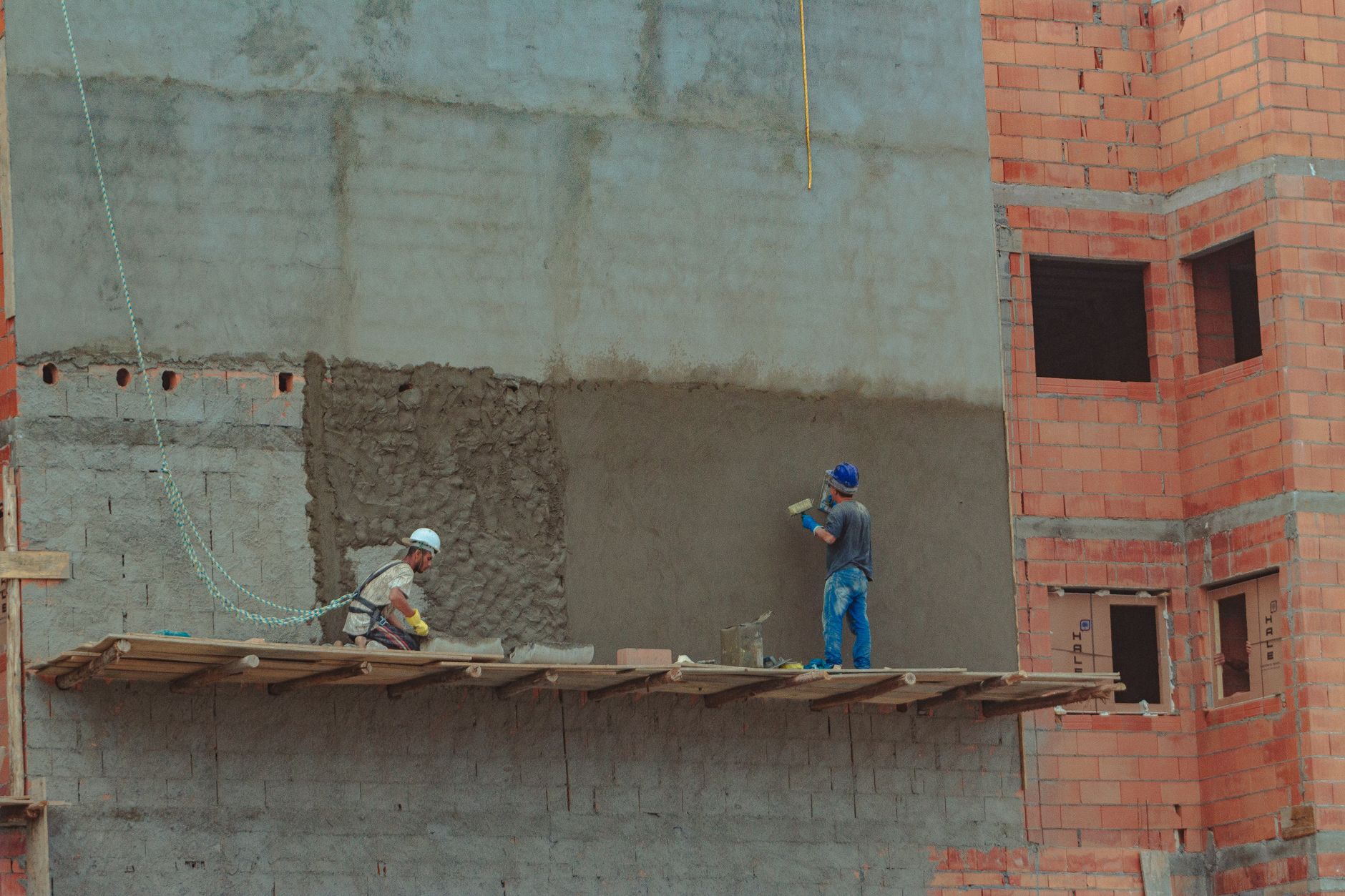 Exterior of industrial construction with wooden site on brick wall and builders in protective hard hats
