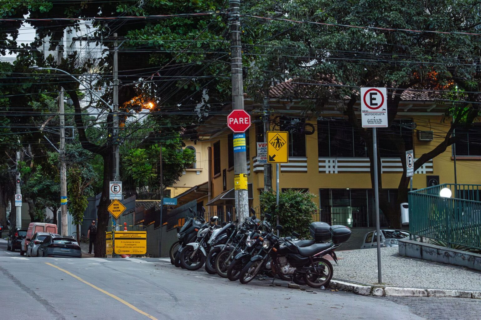 Motorcycles parked on a street in Belo Horizonte, Brazil, with various street signs.