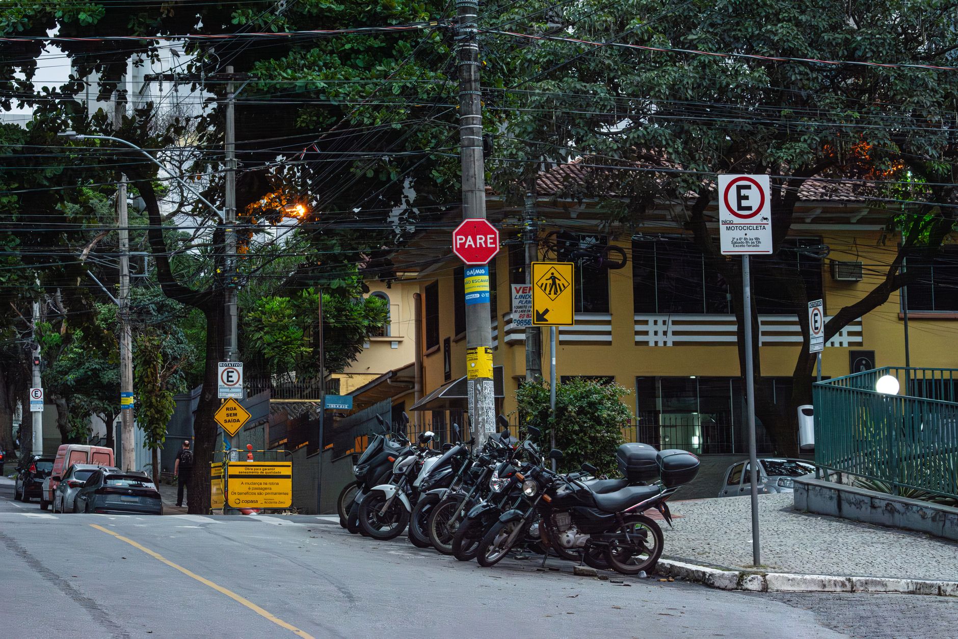 Motorcycles parked on a street in Belo Horizonte, Brazil, with various street signs.