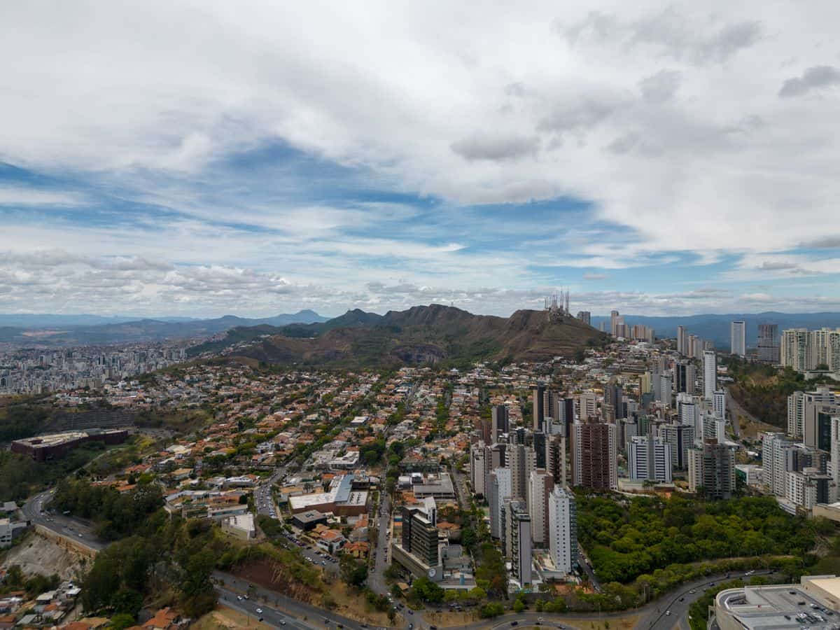 Aerial view of Belo Horizonte featuring the city's skyline and Serra do Curral mountain range under a partly cloudy sky.