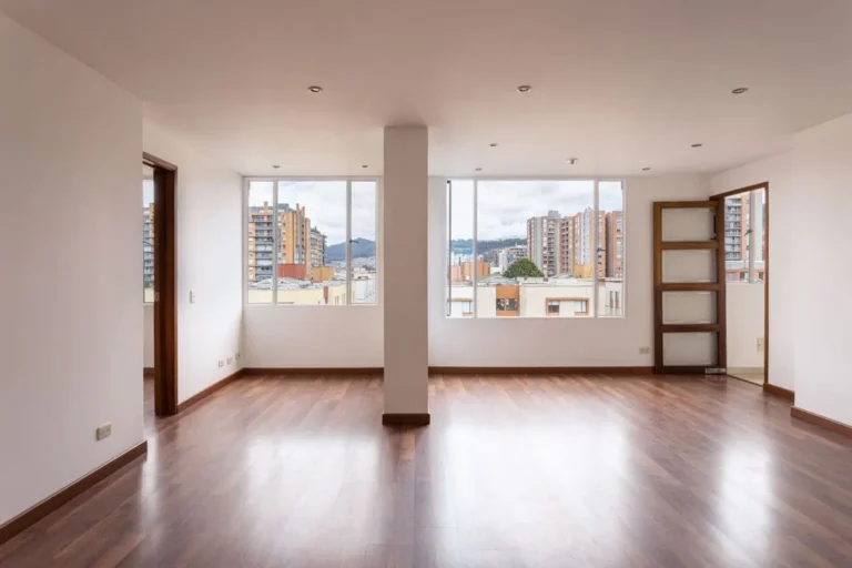 An empty, bright apartment interior showcasing wide windows and wooden flooring.