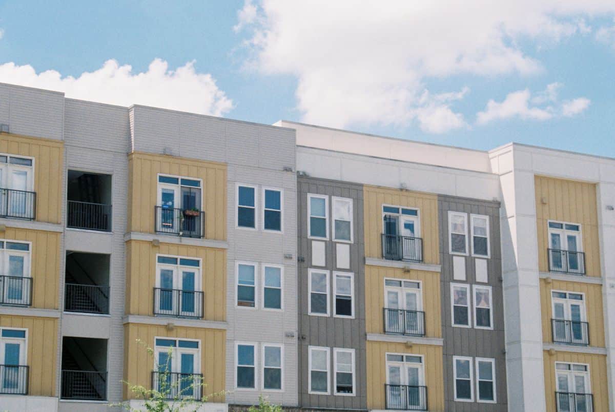 Contemporary apartment building exterior with yellow and grey panels under a clear blue sky.