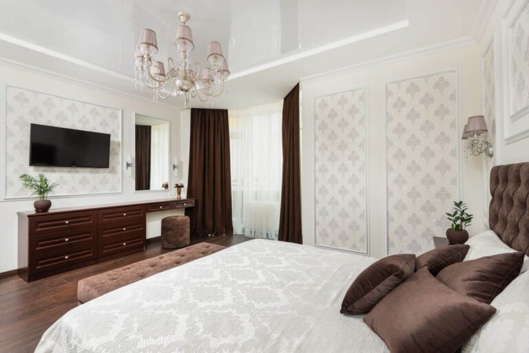 Spacious bedroom featuring luxurious design elements like plush pillows, chandelier, and dresser.
